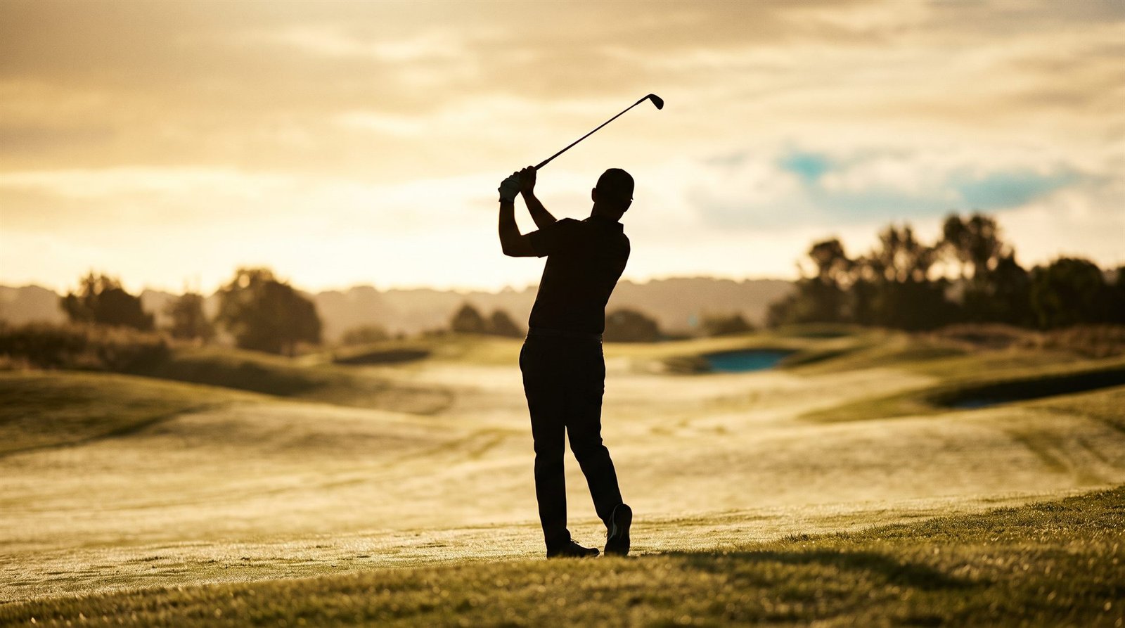 Silhouette d'un golfeur en fin de swing sur le parcours, au coucher du soleil